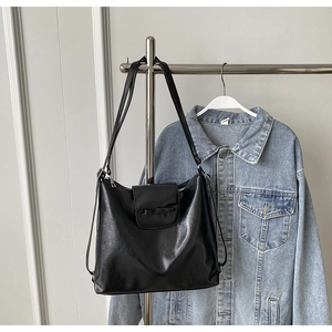 Detalle de bolso tote negro con lazo colgado sobre una chaqueta vaquera azul
