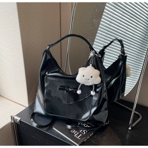 Detail of black glossy hobo bag with bow pocket and plush cloud charm accent