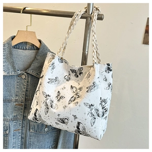 Detail of white tote bag featuring black butterfly prints and beige braided shoulder straps