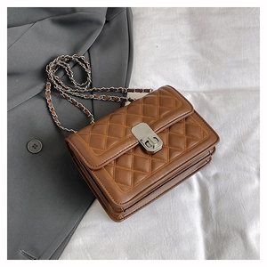 Detail of brown quilted crossbody bag with silver chain strap and metal lock closure
