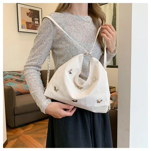 Detail shot of a white pleated tote bag featuring delicate 3D metal butterfly decorations