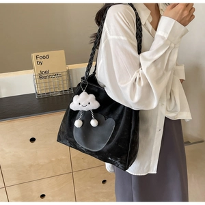 Détail d'un sac cabas noir avec un porte-clés nuage pelucheux et bandoulière tressée