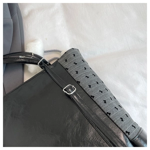 Close-up of black glossy leather tote bag with embroidered bow trim and plush pompom charm