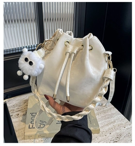 Detail of white lychee leather bucket bag with woven strap and plush doll charm