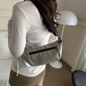 Minimalist light khaki nylon crossbody bag with adjustable black strap in a cozy home setting