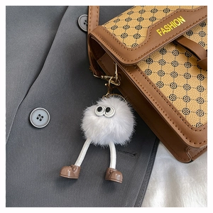 Gros plan du pendentif monstre blanc en peluche avec petites chaussures sur un sac