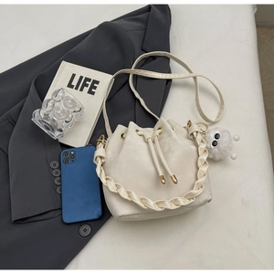 Detail of cream drawstring bucket bag with woven handle and plush charm on casual outfits
