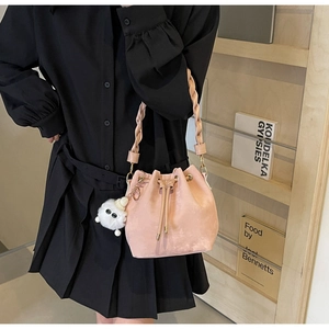 Detail of pink drawstring bucket bag featuring a woven strap and cute plush charm