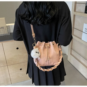 Pink drawstring bucket bag with textured suede finish and fuzzy plush charm accessory