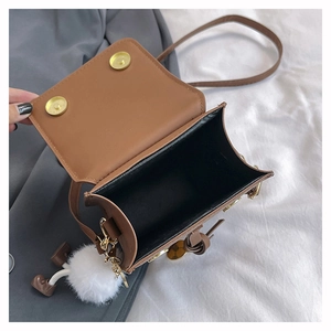 Détail d'un sac bandoulière en cuir marron avec fermoir magnétique et breloque pompon