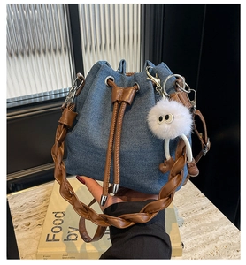 Detail of denim bucket bag with brown leather drawstring and white plush charm on books