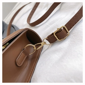 Détail macro d'une bandoulière en cuir marron avec boucle dorée et coutures précises