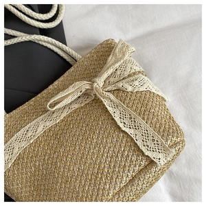 Detailed view of woven straw bag with delicate white lace bow decoration and braided handles