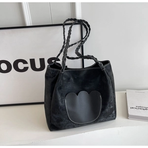 Détail du sac cabas noir avec poche vague et poignées tissées dans un studio minimaliste