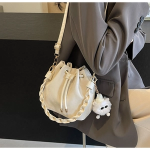 Detail of cream drawstring bucket bag with woven handle and plush charm on a grey suit