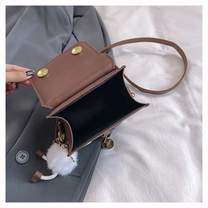 Détail d'un petit sac bandoulière marron en cuir PU avec boutons dorés et pompon blanc