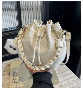 Dettaglio della borsa a secchiello bianca intrecciata con texture in pelle e ciondolo