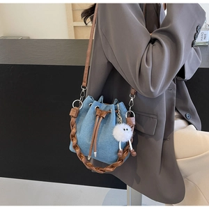 Detail of denim bucket bag with woven handle, drawstring closure and plush pendant charm