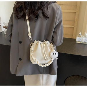 Detail of cream drawstring bucket bag showing woven handle and plush charm detail