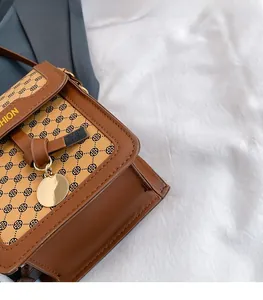 Détail du sac bandoulière marron à motif trèfle avec breloque dorée sur tissu blanc