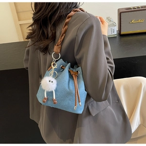 Detail of light blue denim bucket bag with brown leather drawstring and plush charm
