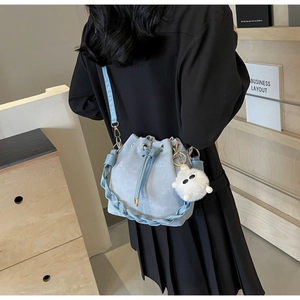 Detail of light blue bucket bag with woven handle and cute white plush charm on a model