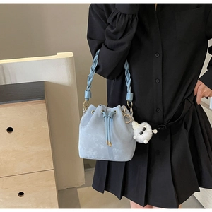 Detail of light blue suede bucket bag with woven handle and fluffy eye charm detail