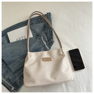 Detail of beige waffle textured tote bag with leather strap and logo patch on fabric