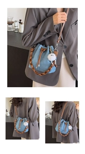 Detail of denim bucket bag with brown woven handle and soft white plush charm