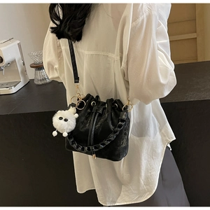 Detail of black drawstring bucket bag with pleated design and plush monster charm