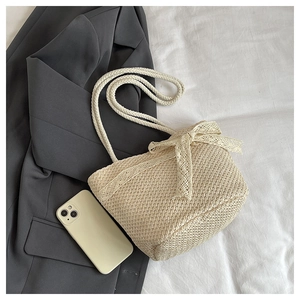 Close-up of beige woven straw tote bag with elegant lace bow detail on white fabric