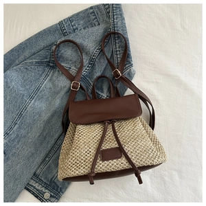 Close-up of small woven straw backpack with brown leather trim on white bedding