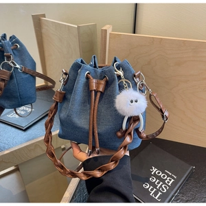 Detail of blue denim bucket bag featuring brown leather drawstring and braided handle strap