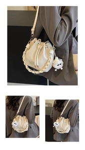Detail showing creamy white leather bucket bag with woven handle and plush monster charm