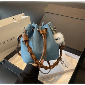 Detail of denim bucket bag with woven handle and plush monster charm on black gift box