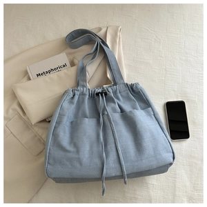 Detailed view of light blue denim tote bag with drawstring closure and front pockets