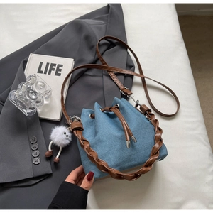 Detail of denim bucket bag with drawstring closure, leather handle, and plush charm