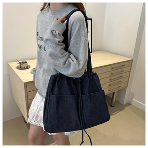 Detail of large denim tote bag featuring dual front drawstring pockets and shoulder strap