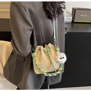 Detail of straw woven bucket bag with green faux leather drawstring and plush eye charm