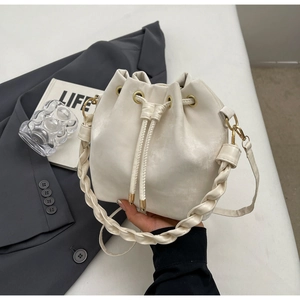 Detail view of cream drawstring bucket bag with woven handle and gold hardware