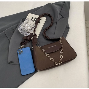 Detail of dark brown shoulder bag with decorative petal chain and woven handle on blazer