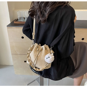 Detail of hand-woven straw bucket bag featuring a drawstring closure and plush pompom charm