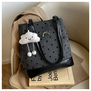 Detailed view of grey polka dot tote bag with a plush cloud charm on a beige armchair