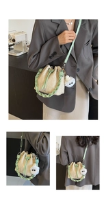 Detail view of straw bucket bag with green leather trim and plush charm accessory