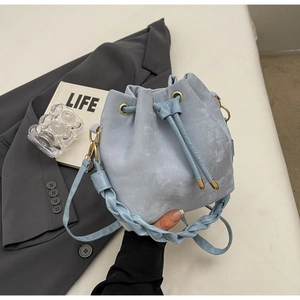 Detail of blue drawstring bucket bag featuring leather texture and woven shoulder strap