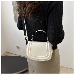 Dettaglio di una borsa a sella crema con cuciture sottili e fibbie in oro lucido