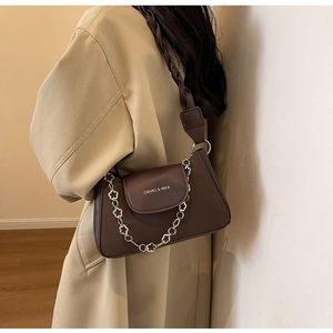 Detail of dark brown leather bag featuring woven strap and silver floral chain ornament