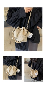 Detail of straw woven bucket bag featuring drawstring closure and fluffy pompom charm