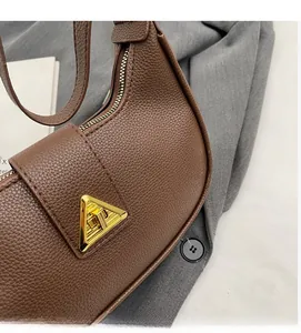 Détails du cuir litchi marron foncé et du fermoir triangulaire doré sur le sac à main