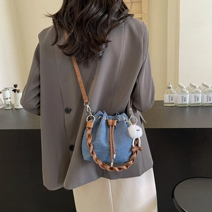 Denim bucket bag with drawstring and plush ball charm, worn as a crossbody shoulder bag